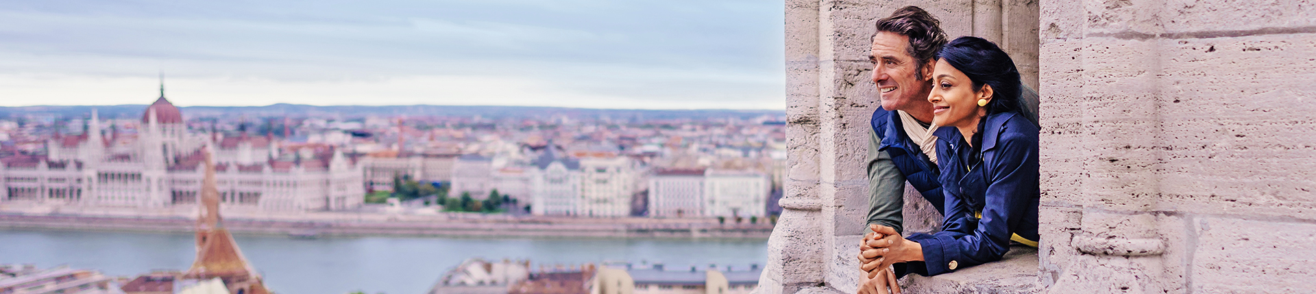 Couple framed by a window overlooking a river and cityscape in Budapest