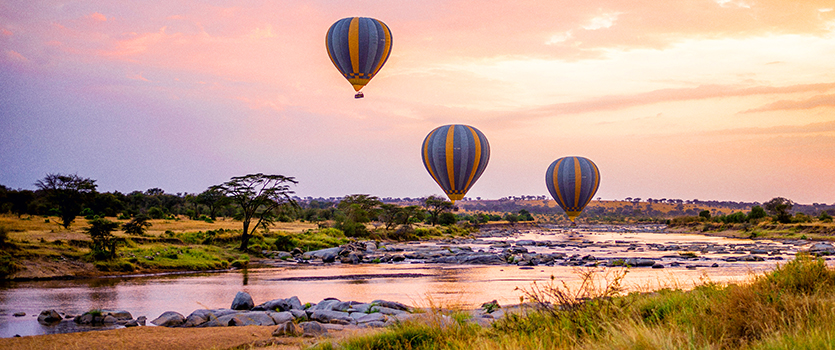 3 hot air balloons landing near a river during sunset in Tanzania